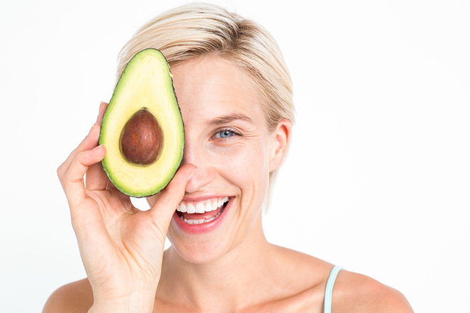 Pretty woman covering her eye with an avocado on white background